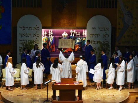 Confirmands in white robes on the bima in front of an open ark.