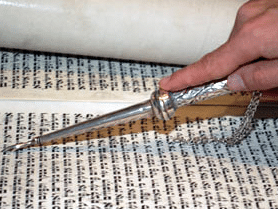 hand with silver pointer reading Torah Scroll