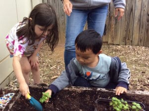 two children planting things in a raised bed garden
