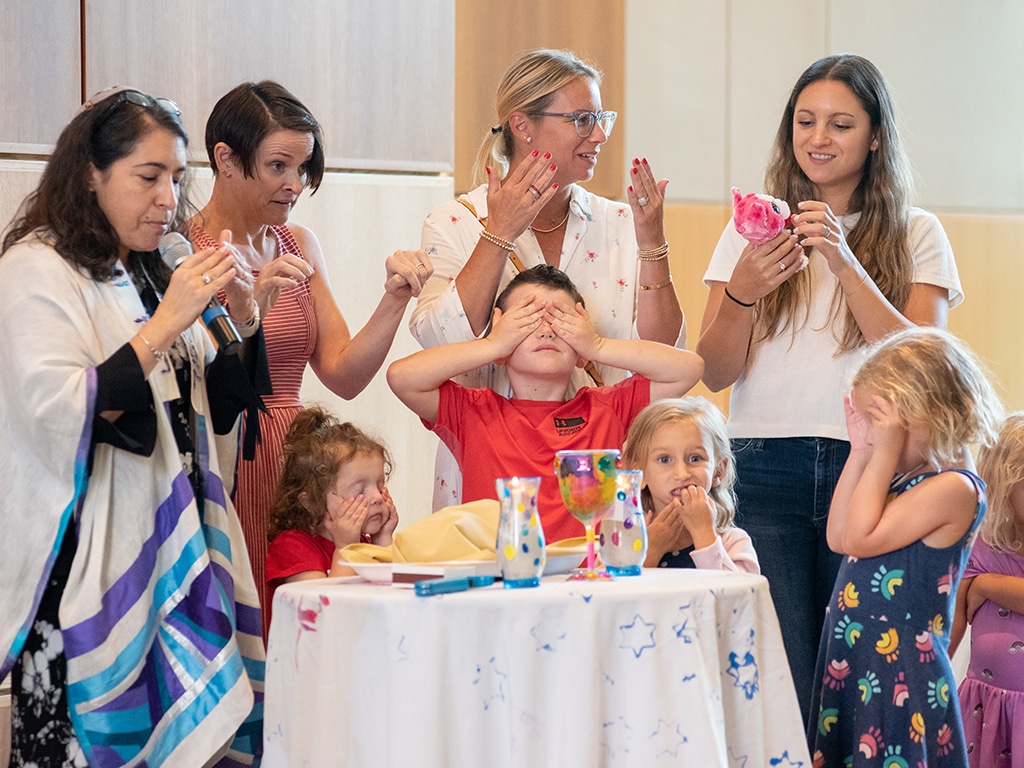 toddlers light Shabbat candles with Rabbi Shankman and others.