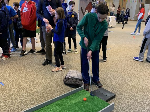 Child using a putting green during Purim Carnival