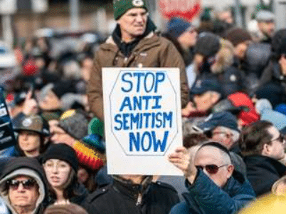 people outside at a rally with man holding a sign saying "Stop antisemitism now"