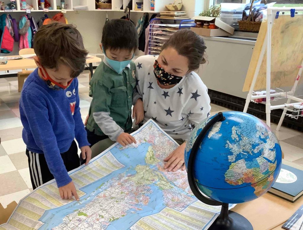 two young boys with masks on read a map with their teacher
