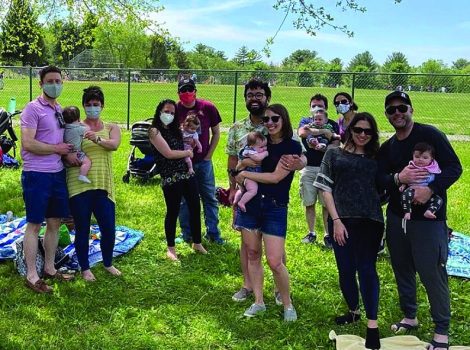 5 couples stand on the grass holding babies