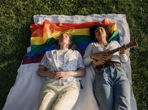 Two women lying down on a picnic blanket with a rainbow pride flag under their heads