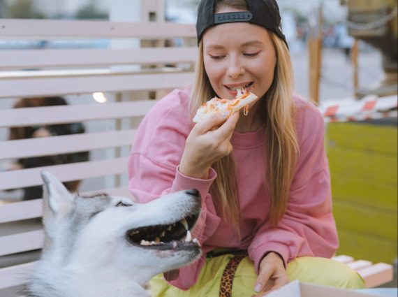 20-something woman eating pizza with her dog