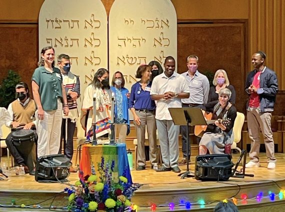 group of people stand on a rainbow-decorated bima