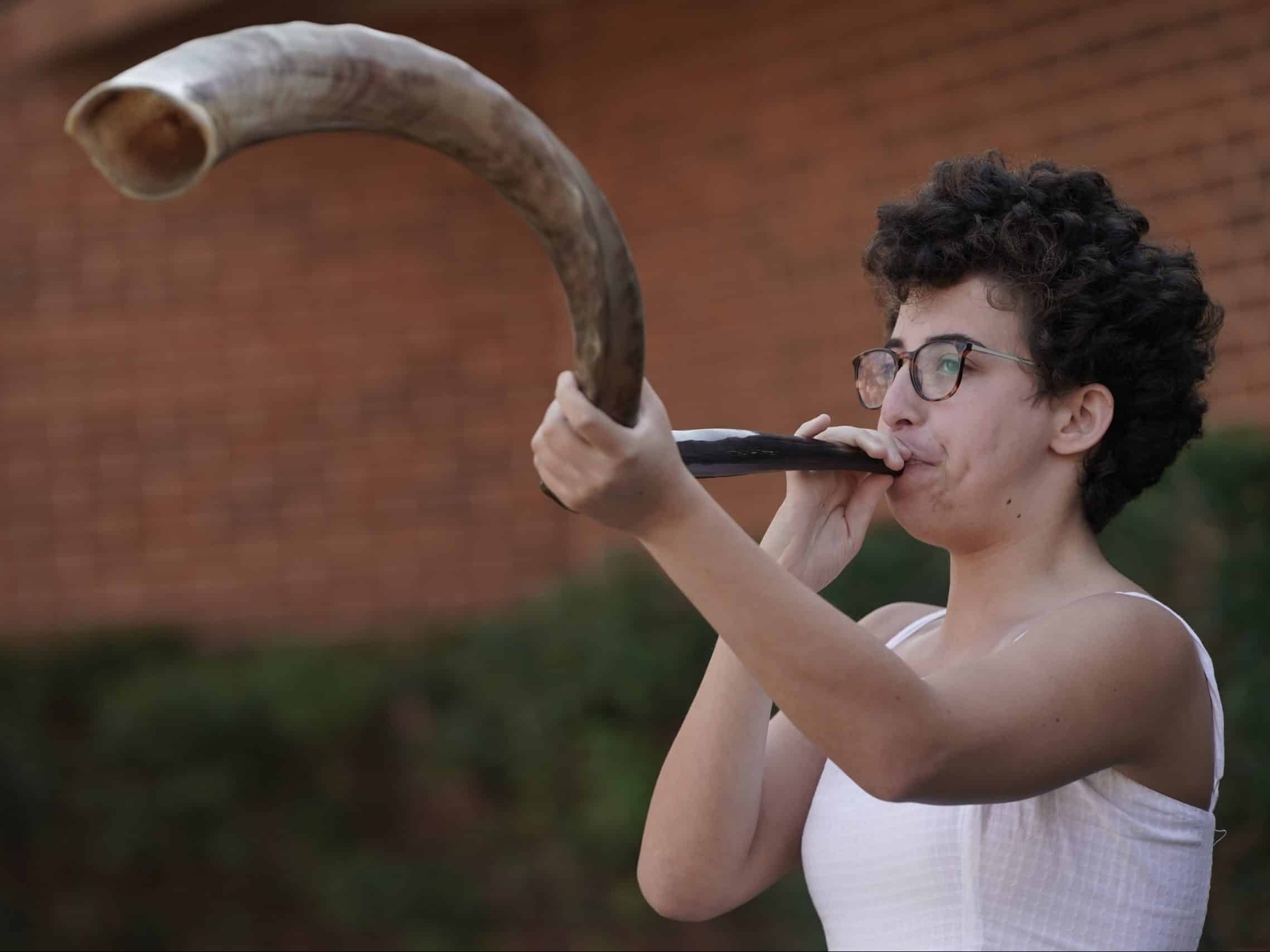 woman blowing a large shofar outside