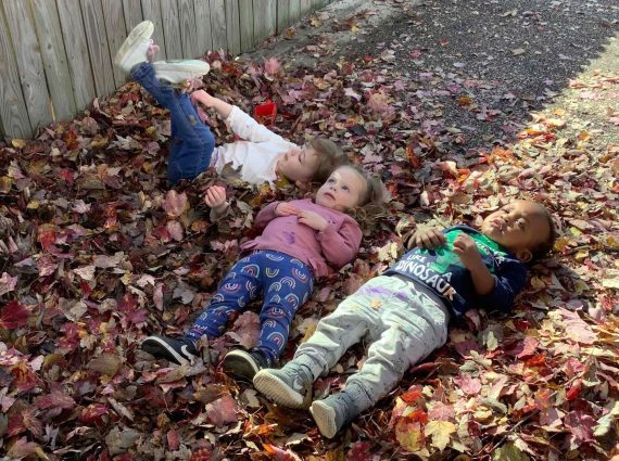 three young children lie in a pile of leaves