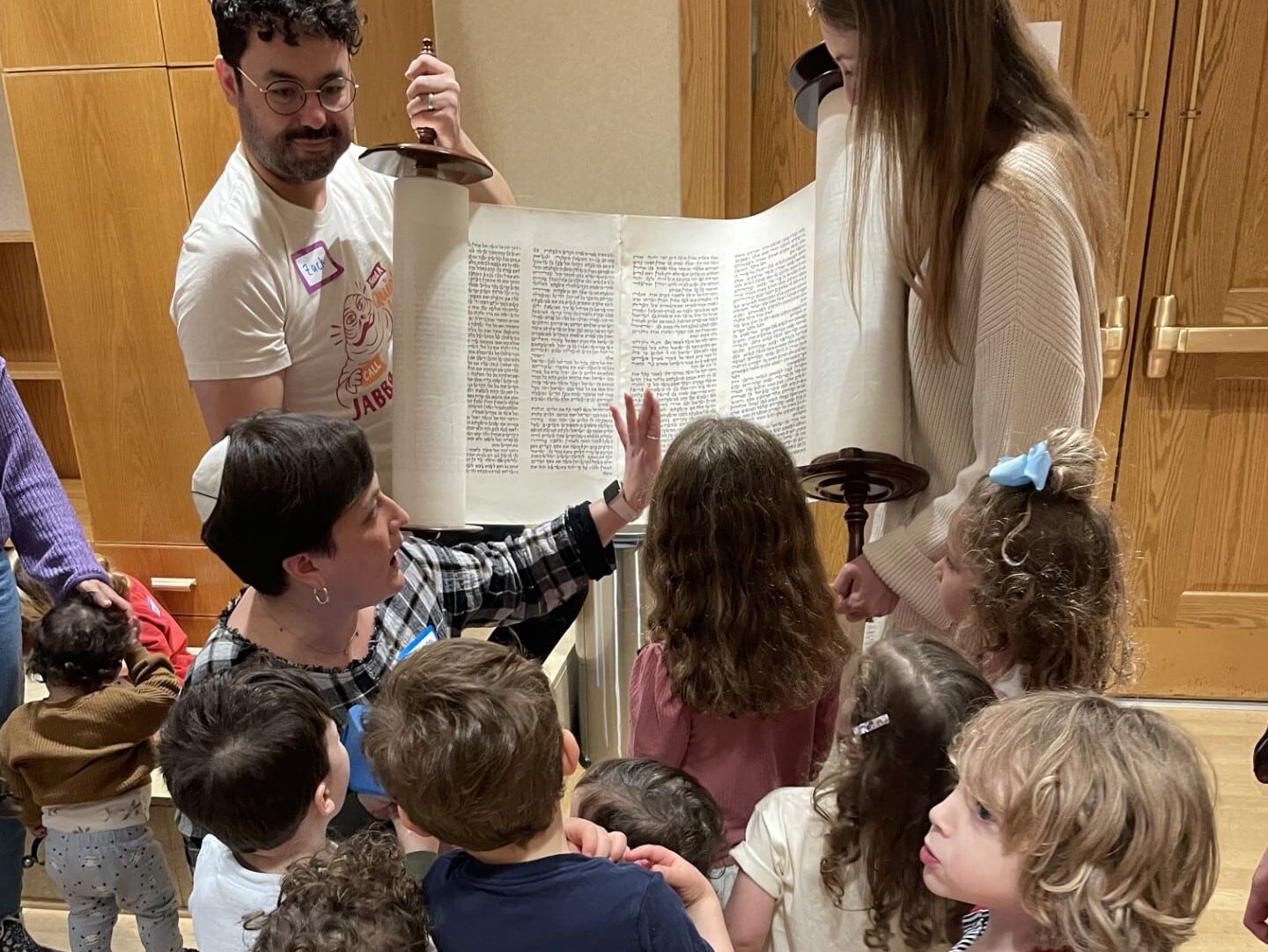 Rabbi Fischel shows a group of young children the Torah that two parents are holding open