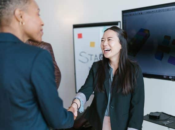 Black woman shaking hands with Asian woman in front of whiteboard