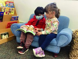 two young children sit on a small couch reading a book