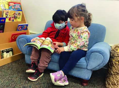 two young children sit on a small couch reading a book