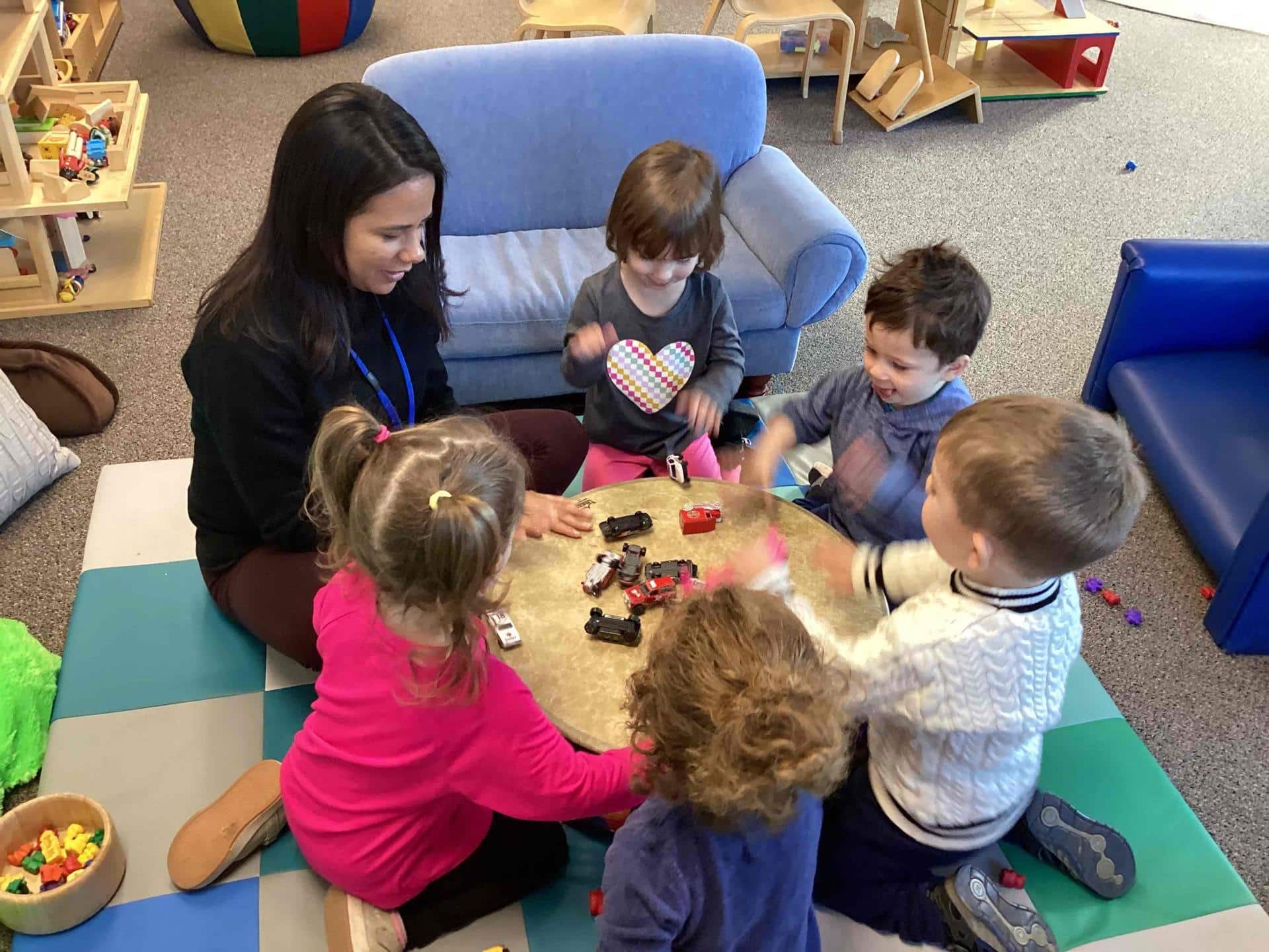 teacher sits at a small round table with 5 toddlers