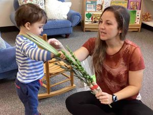 female teacher sits on floor showing a lulav to a child
