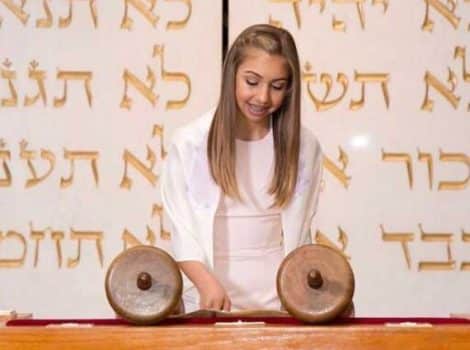 teen girl in white on bima reading a torah scroll