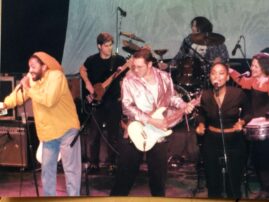Photo of the band "Congregation" onstage with guitarist David Boris in the center wearing a pink satin shirt