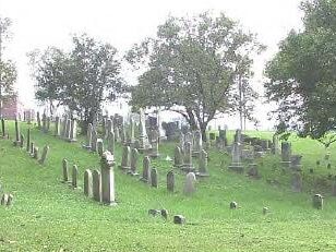 gravestones on a grassy hill with trees in the background