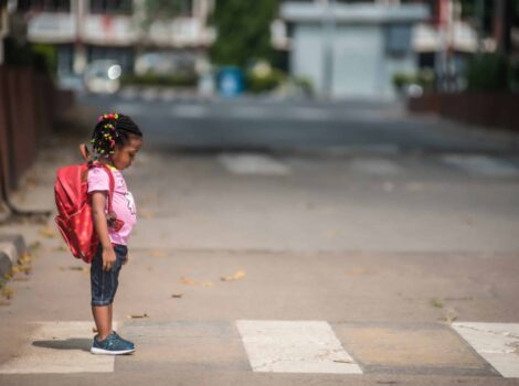 young child with red backpack stands in crosswalk
