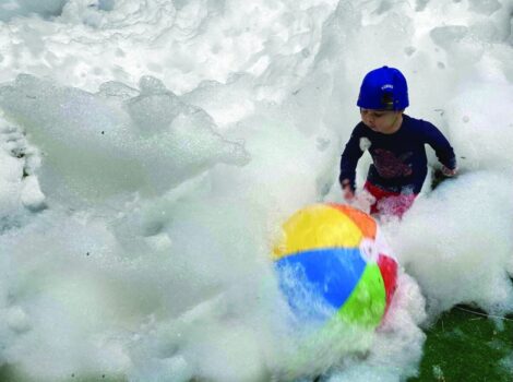 child plays with rainbow beach ball in large pile of bubbles