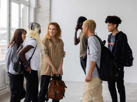 diverse group of college students stand in a white room with large windows