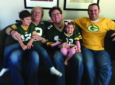 The Schuman family wearing Green Bay Packers gear sit on couch