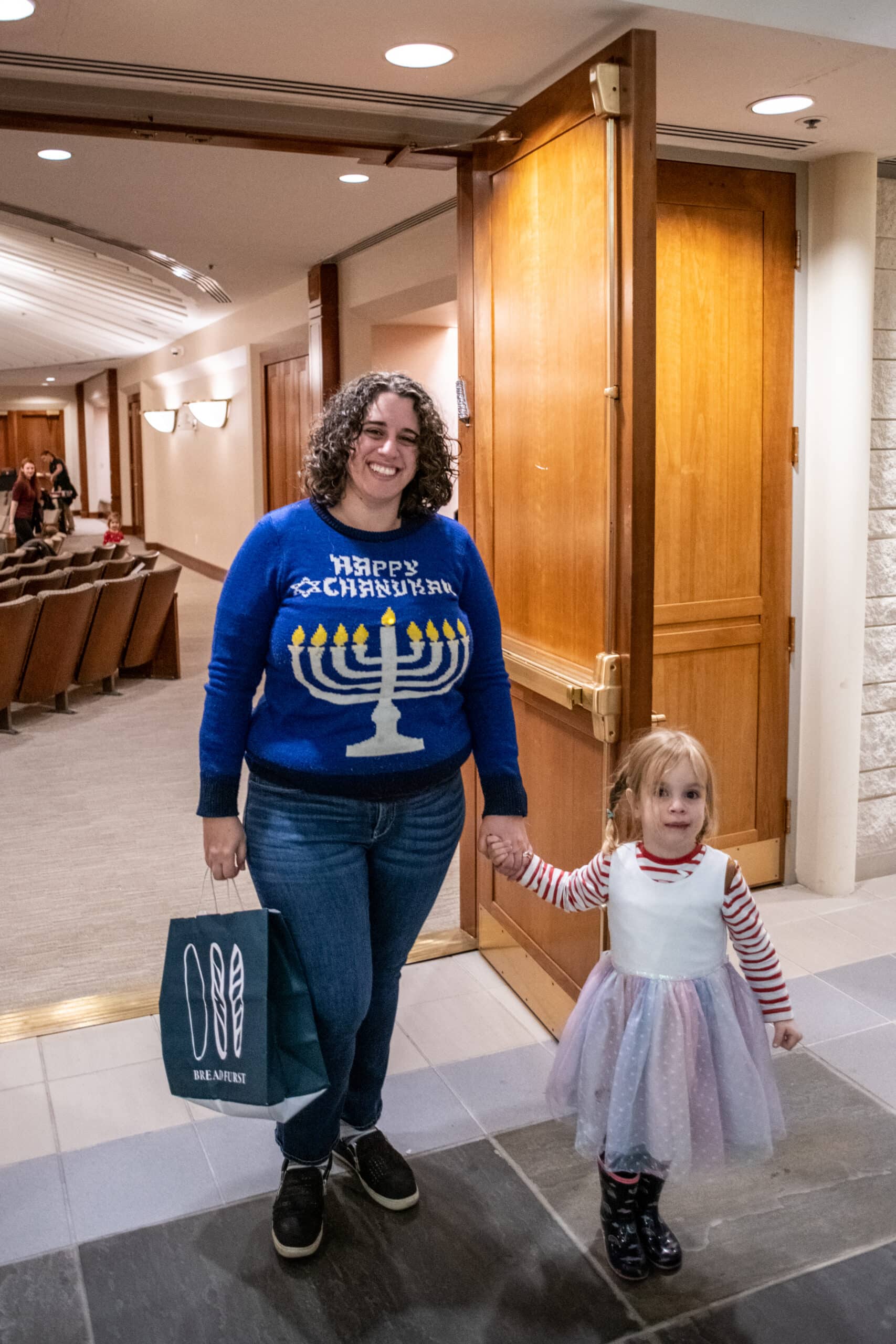 Woman in Hanukkah sweater holds the hand of a young girl