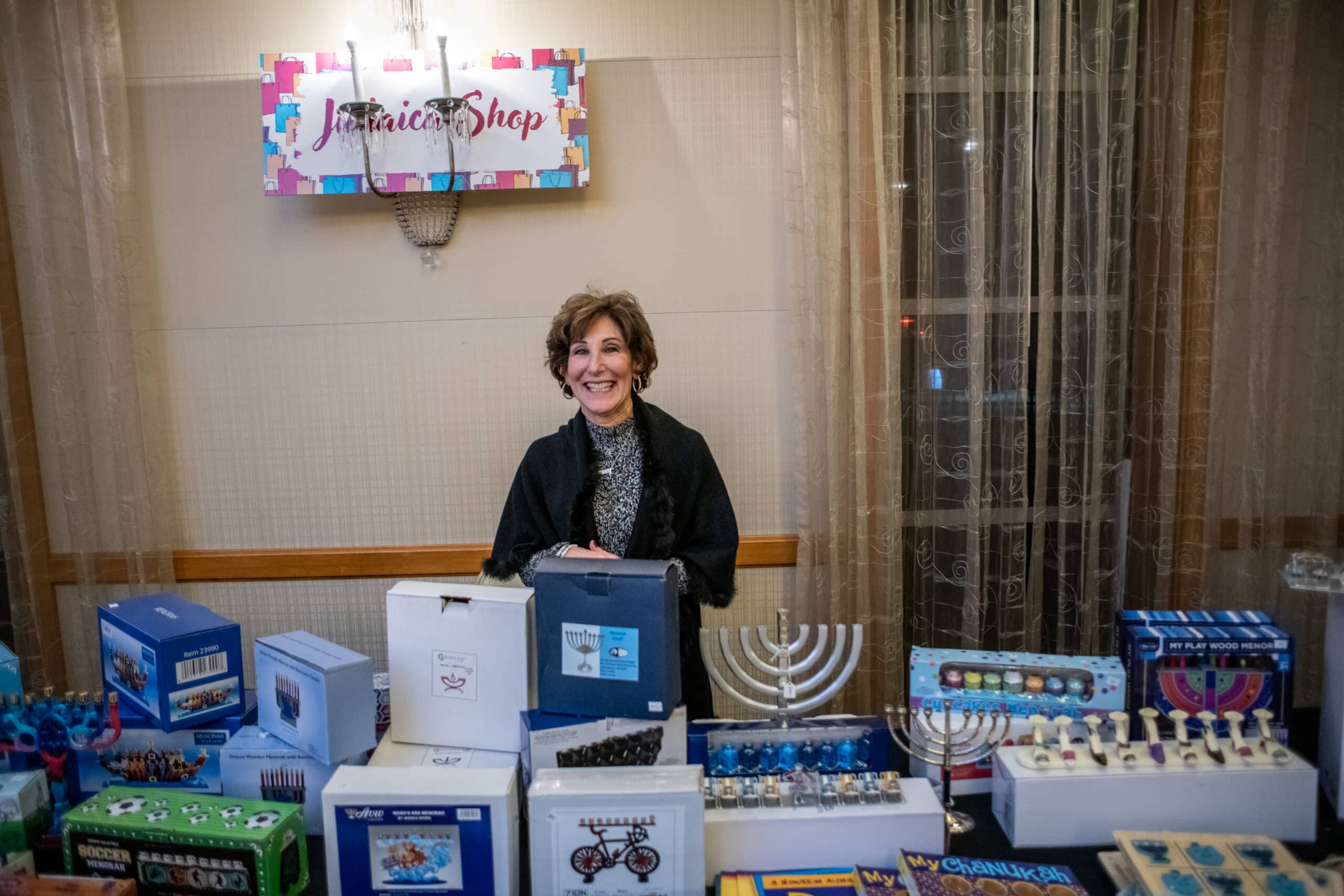 Woman stands behind table filled with Hanukkah products for WWHC Judaica Shop