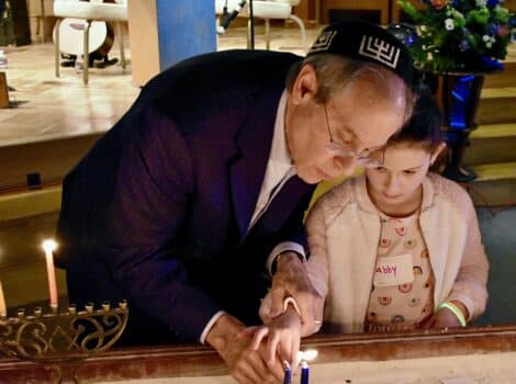Grandfather lights menorah with grandchild at shabbat hanukkah 2023
