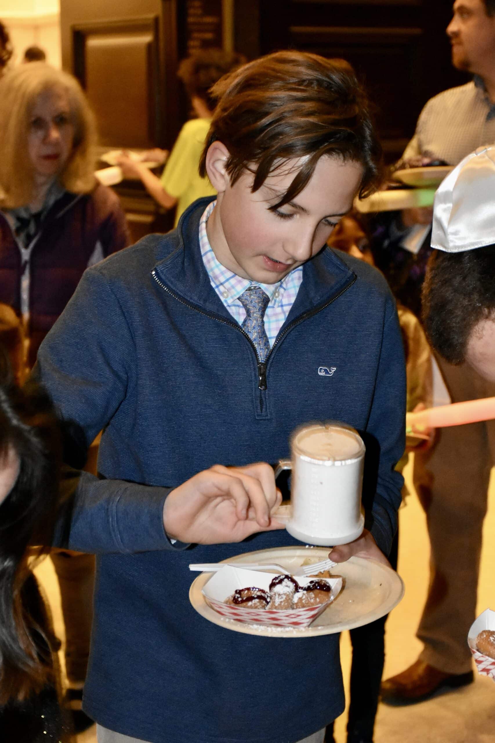 Child sprinkling sugar on donuts at shabbat hanukkah 2023