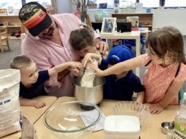 Children pour flour into a bowl with the help of an adult male.