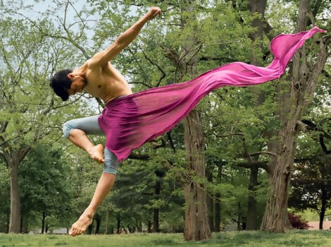 male dancer jumps in the air with pink fabric blowing behind him.
