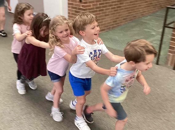 5 children walk in a line with hands on each others' shoulders