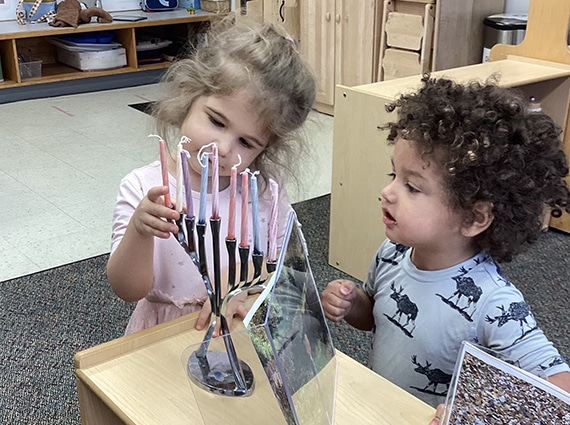 Two young children add candles to a Hanukkiyah