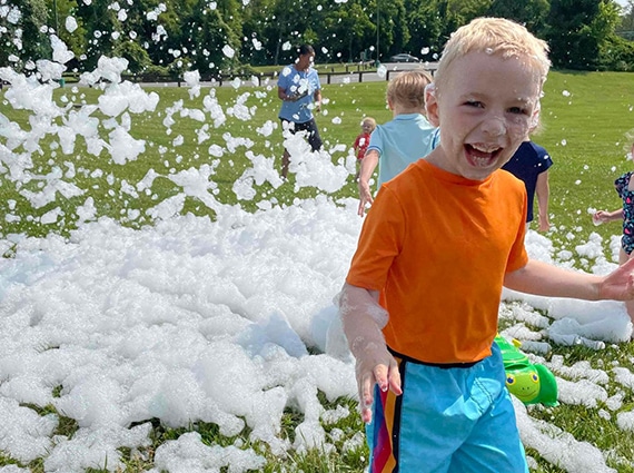 Child in orang shirt plays in front of a pile of foam bubbles