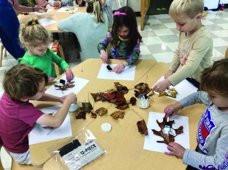 children sit around a table working on an art project with leaves
