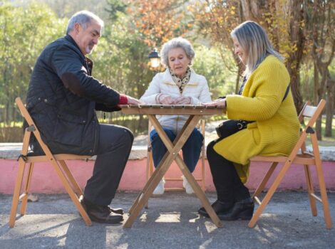 Senior man and two senior women sit outside around a small table