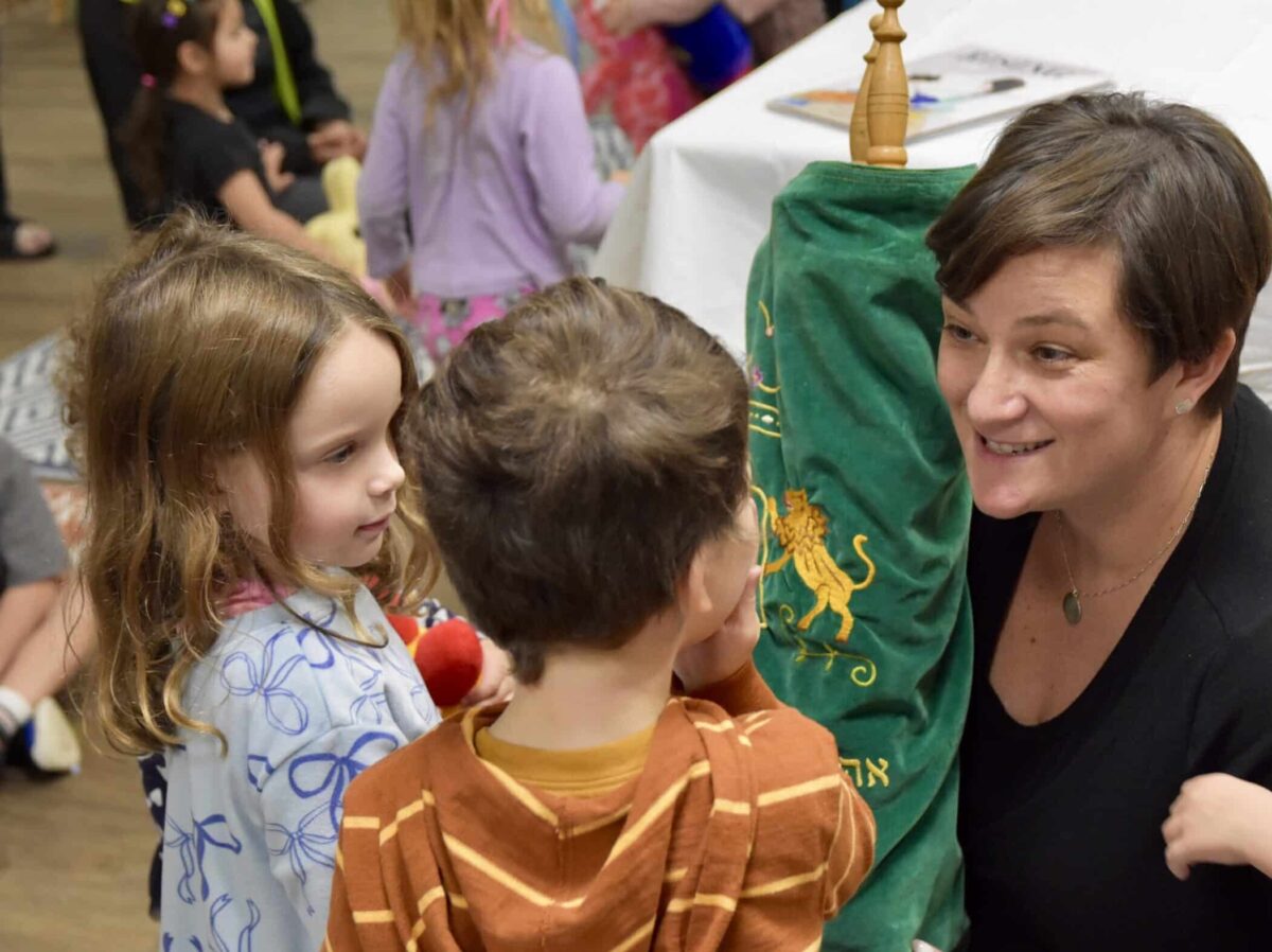 Two young children look on as Rabbi Fischel holds a torah