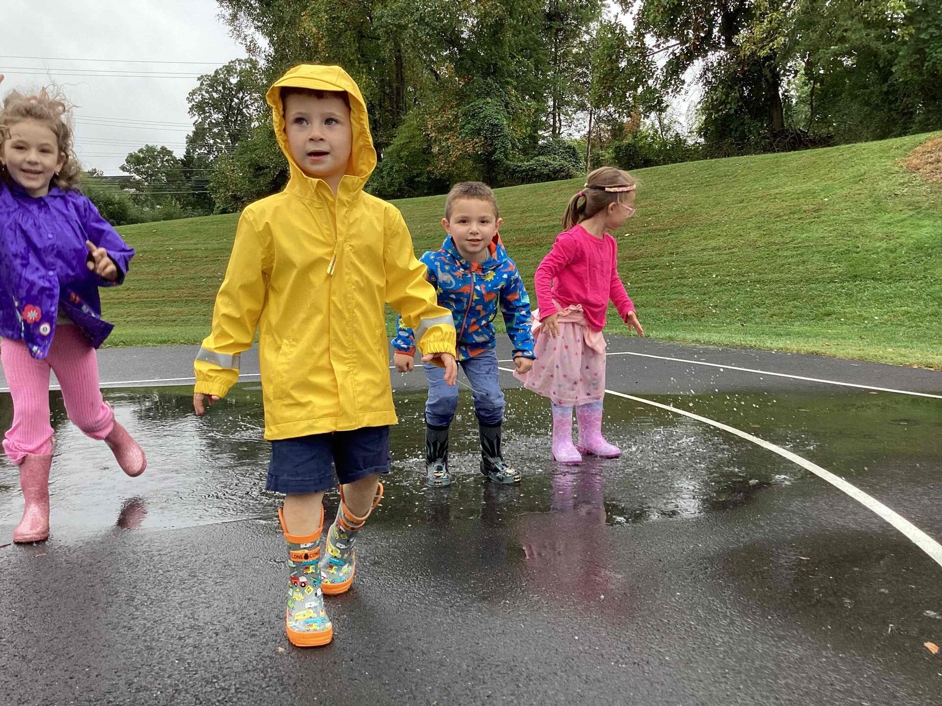 children in raingear walk through puddles