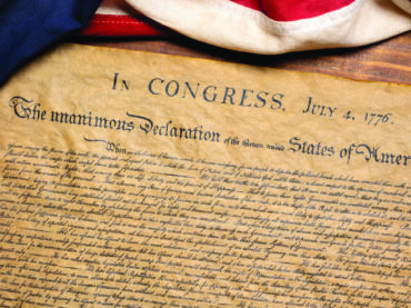 Declaration of Independence on parchment with US flag draped over the top