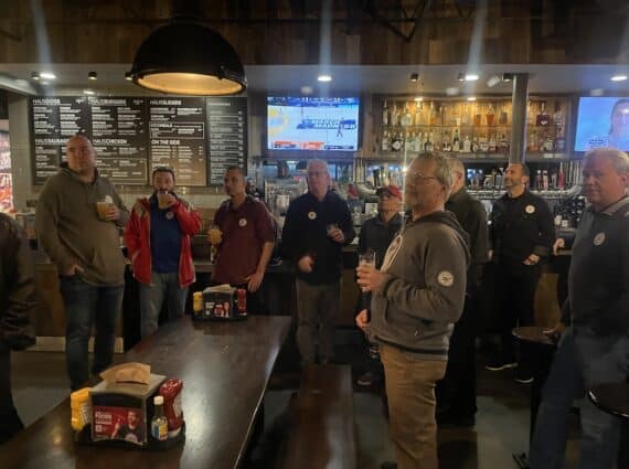 Men standing in a bar while basketball shows on the TV