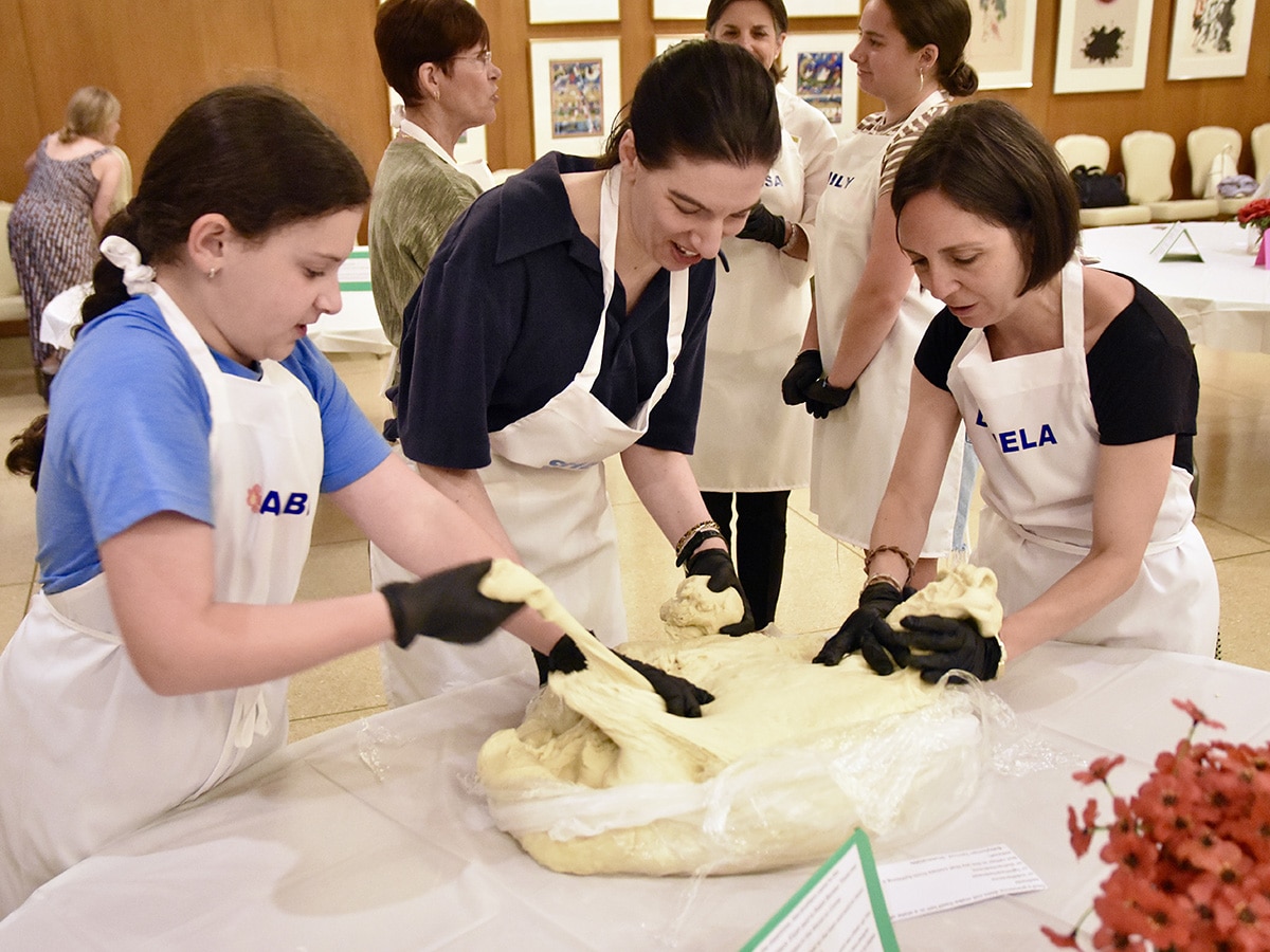 Three women in aprons pulling out challah dough
