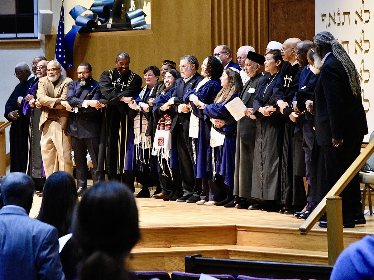 Interfaith clergy members hold hands while on the bimah for MLK Shabbat