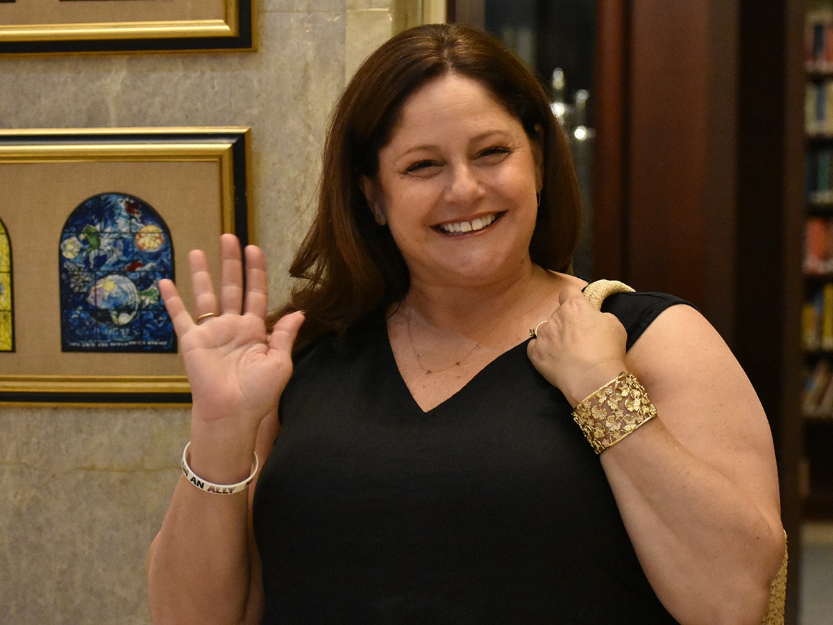 Woman in black dress smiles and waves at the camera