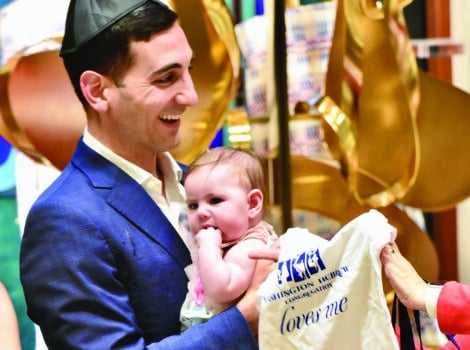 Young father in a suit holds his newborn as he is handed a WHC onesie